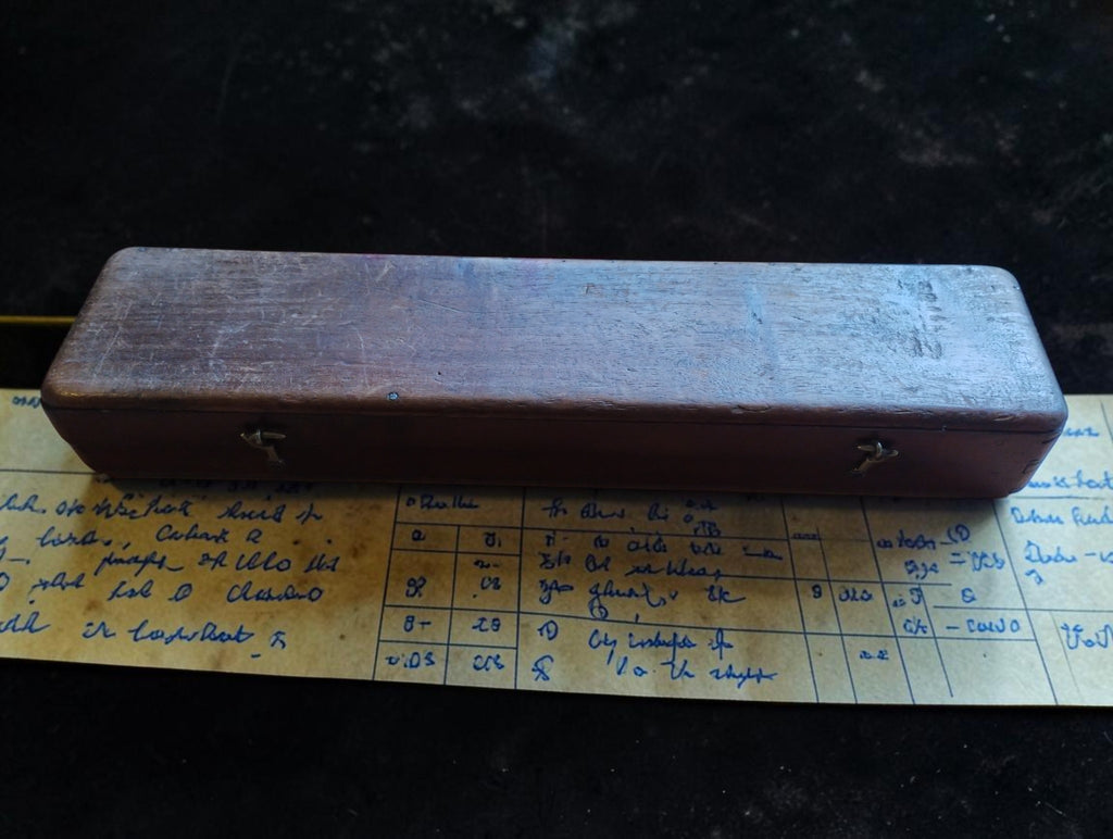 Closed wooden instrument case with two front clasps, shown resting on the handwritten historic correction table.
