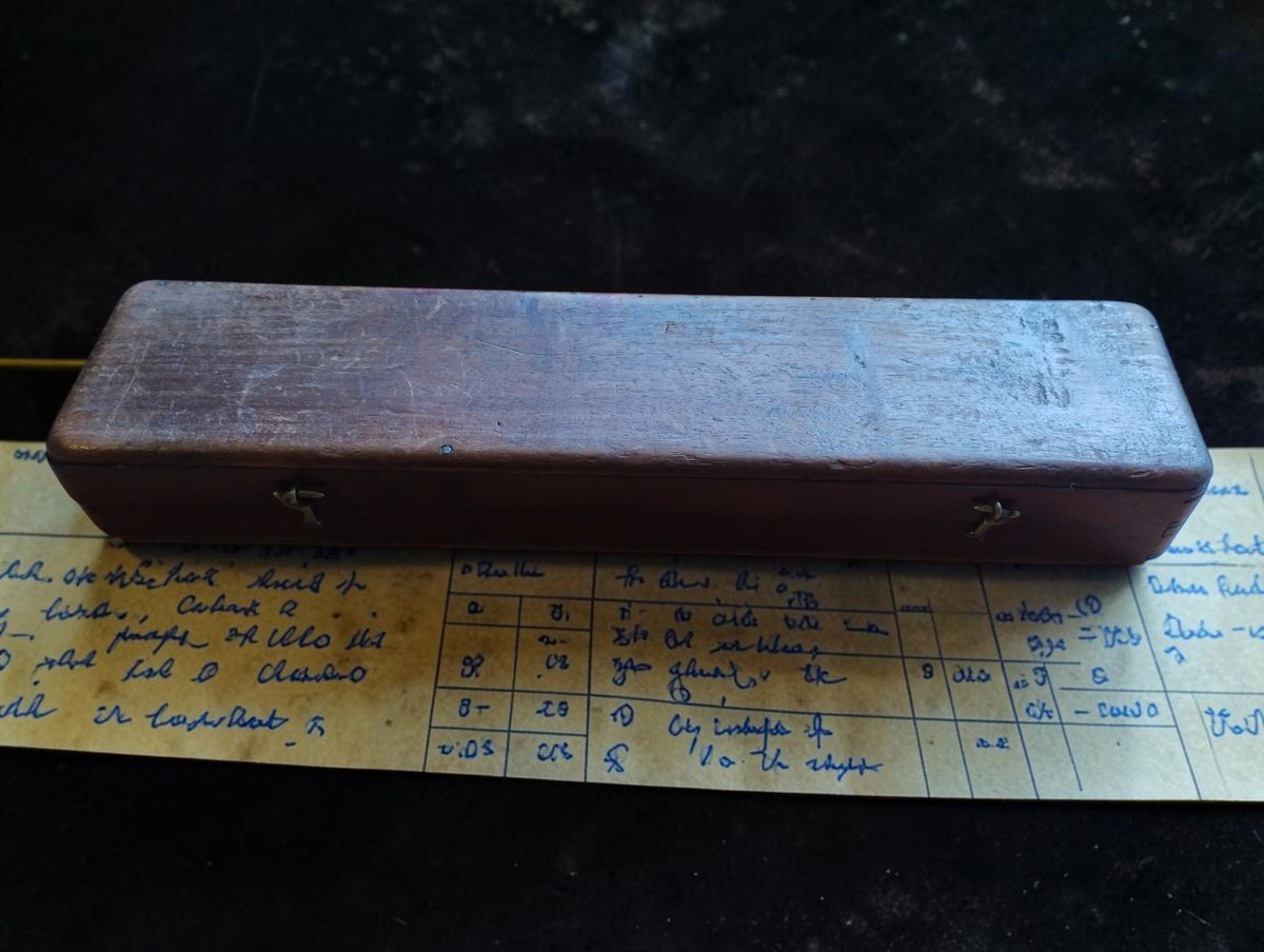 Closed wooden instrument case with two front clasps, shown resting on the handwritten historic correction table.
