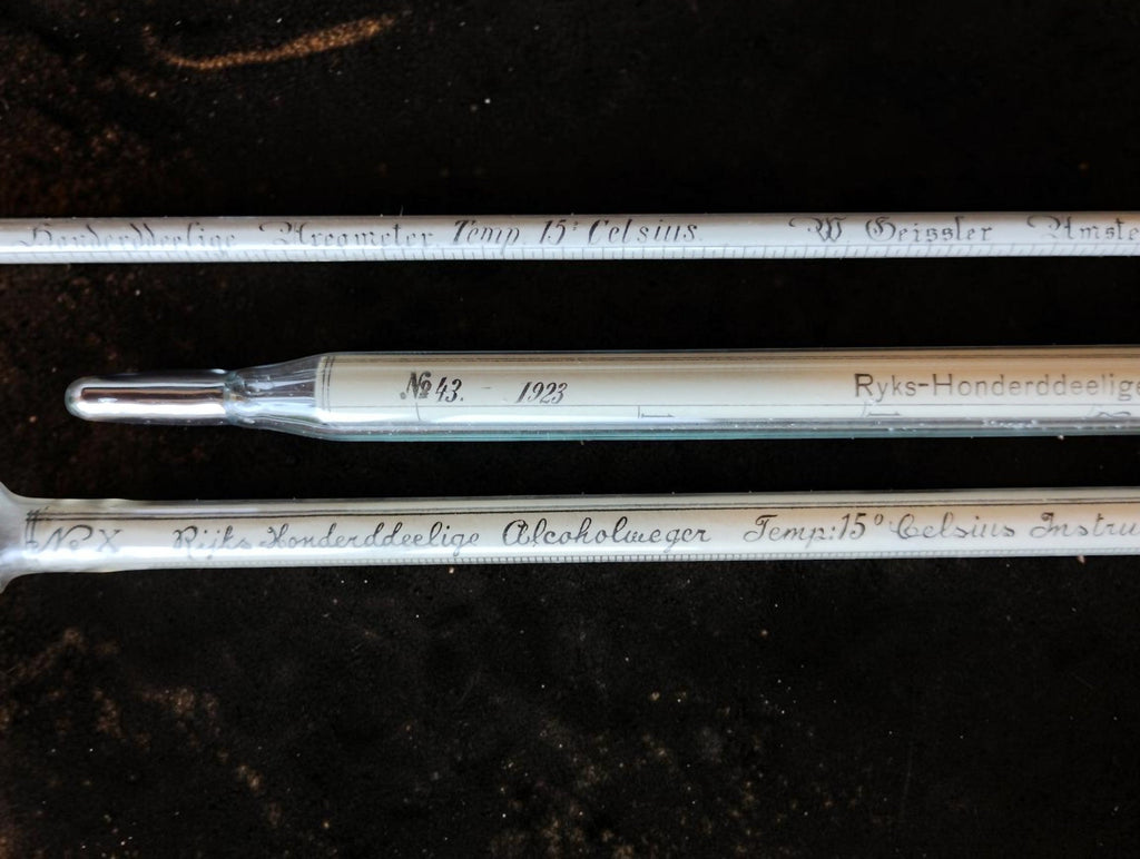Close-up of the glass measuring instruments with handwritten inscriptions and the thermometer's metal-covered tip.
