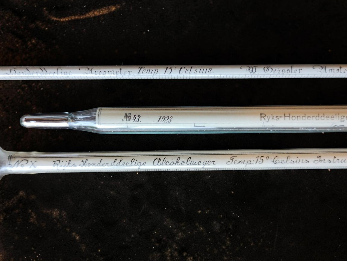Close-up of the glass measuring instruments with handwritten inscriptions and the thermometer's metal-covered tip.
