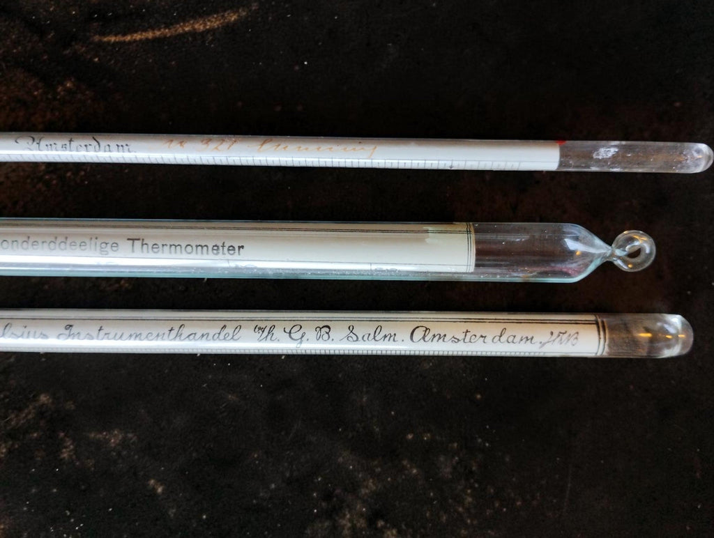 Close-up of the glass instrument ends and suspension loop in the antique Dutch measuring set.
