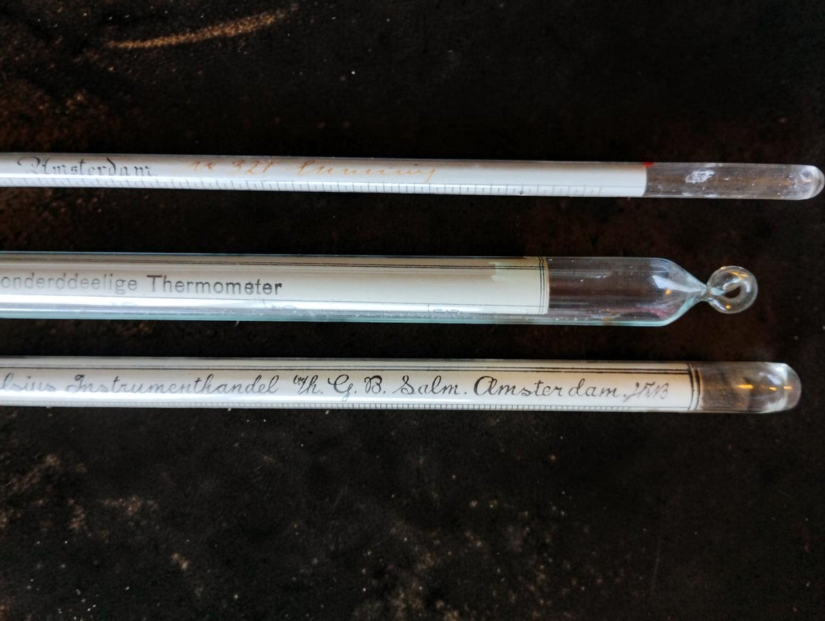 Close-up of the glass instrument ends and suspension loop in the antique Dutch measuring set.
