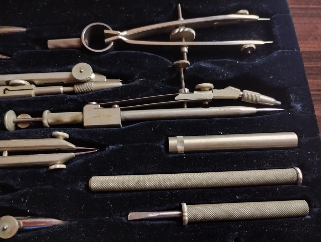 Close-up of adjustable compasses, metal accessories and textured handles inside the drafting instrument case.
