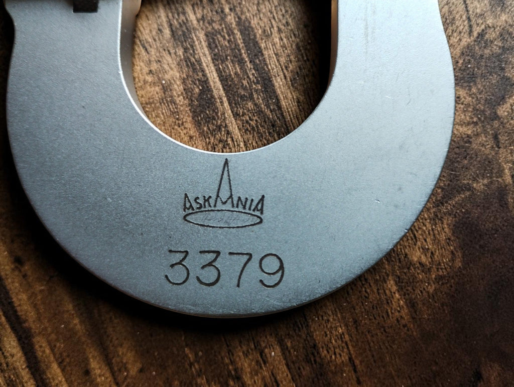 Close-up of the Askania logo and number 3379 on the matte metal micrometer frame.
