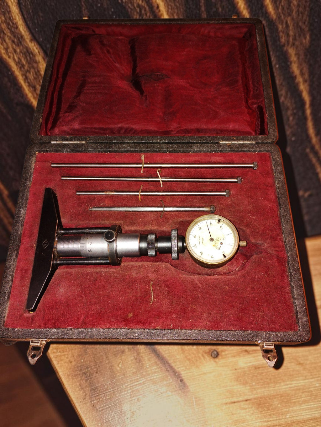 Vintage depth micrometer with dial indicator and four measuring rods in a red-lined storage case
