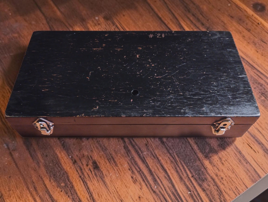 Closed black-painted wooden micrometer case with two metal clasps, handwritten number 24 and visible surface wear.
