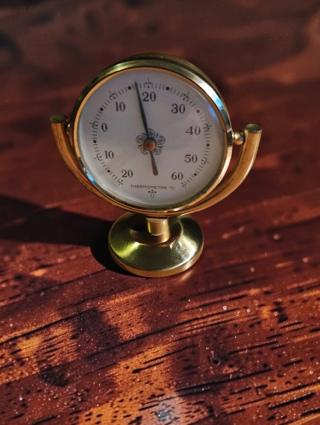 Vintage brass desk thermometer with a French Celsius dial, tilting cradle and round pedestal base.
