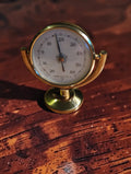 Vintage brass desk thermometer with a French Celsius dial, tilting cradle and round pedestal base.
