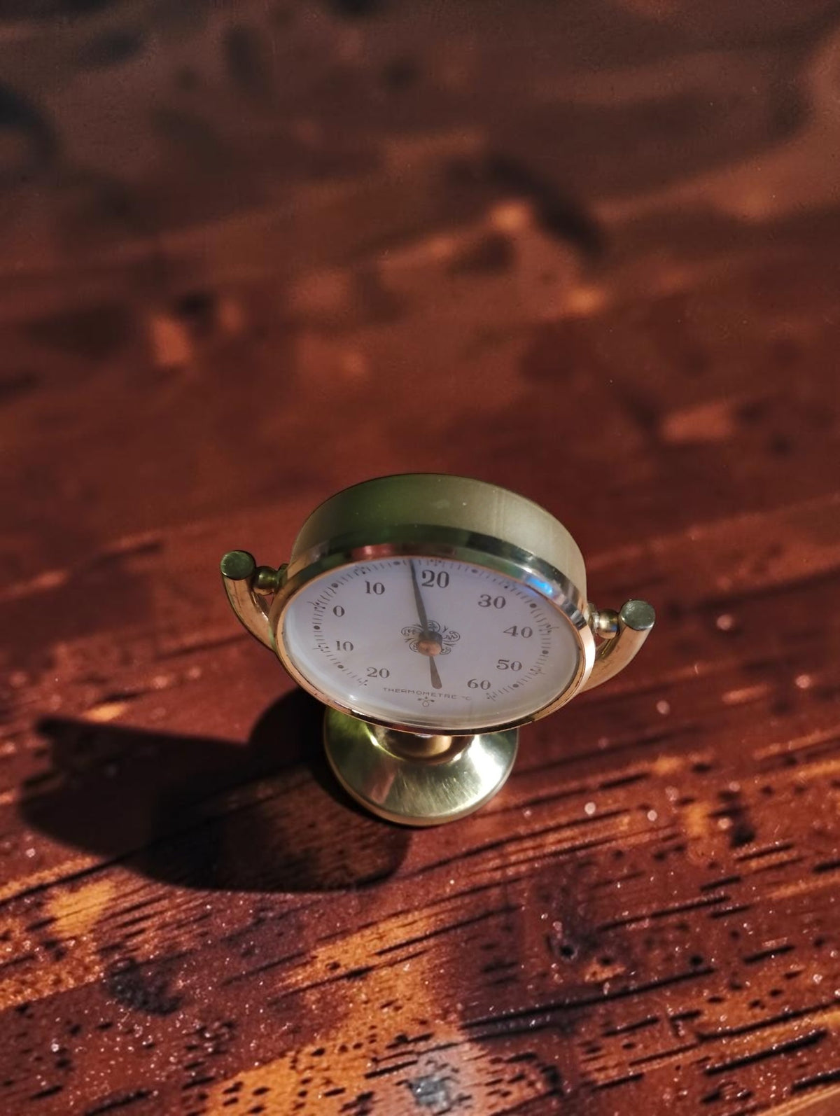 Angled top view of the vintage brass desk thermometer showing its round dial and tilting support.
