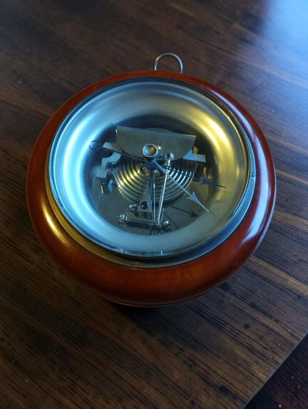 Skeleton aneroid barometer with exposed mechanism, reddish-brown wooden case and hanging ring.

