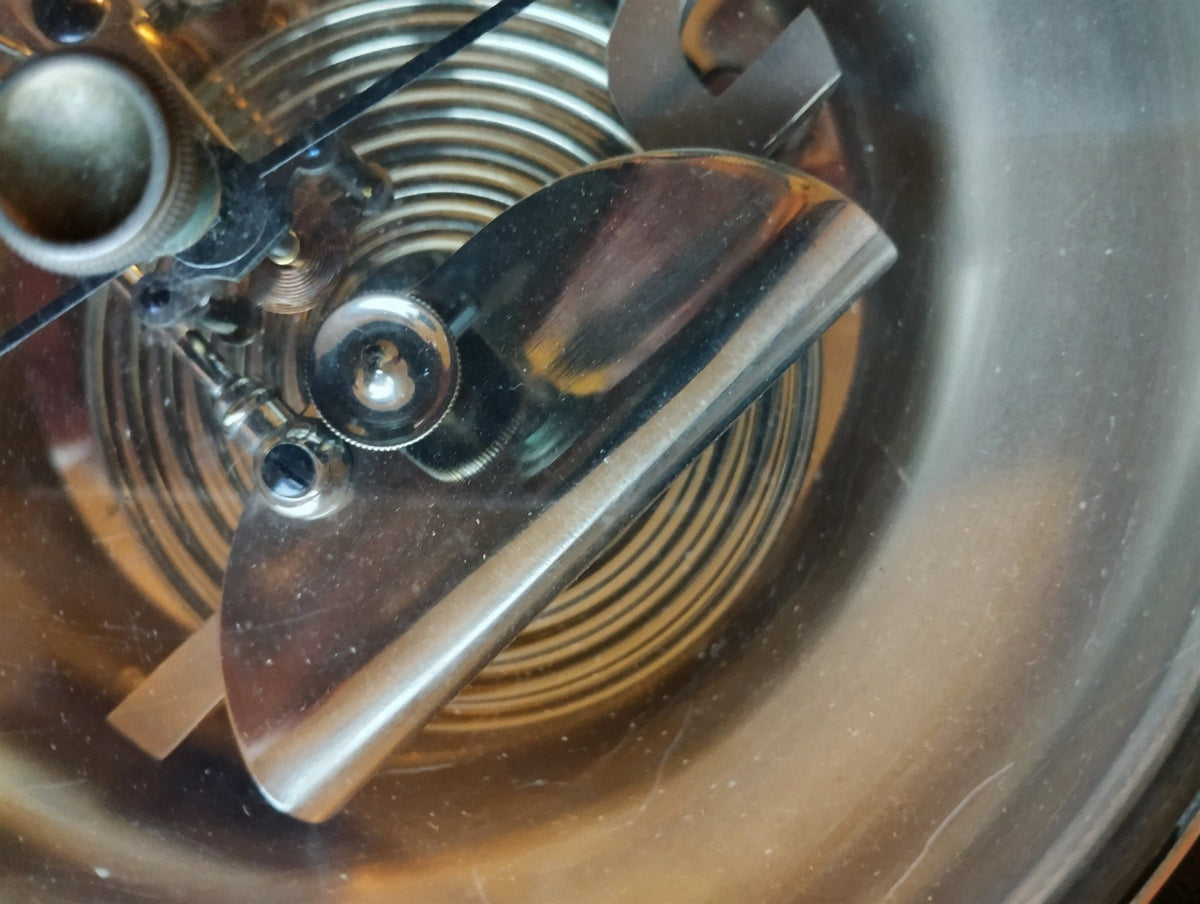 Close-up of the ribbed aneroid capsule and polished metal bridge beneath the barometer glass.
