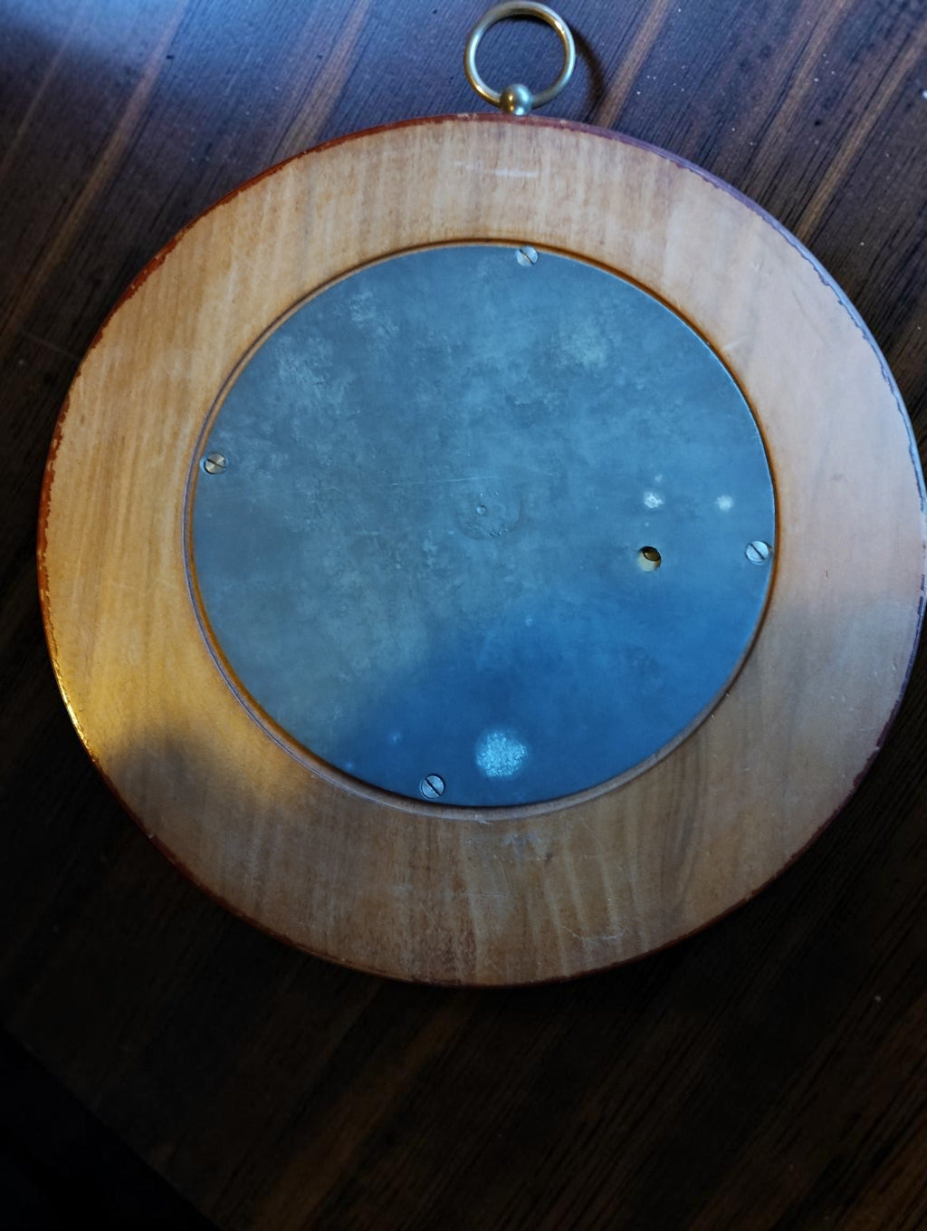 Back of the skeleton barometer with a circular metal cover, fixing screws and surrounding wooden case.
