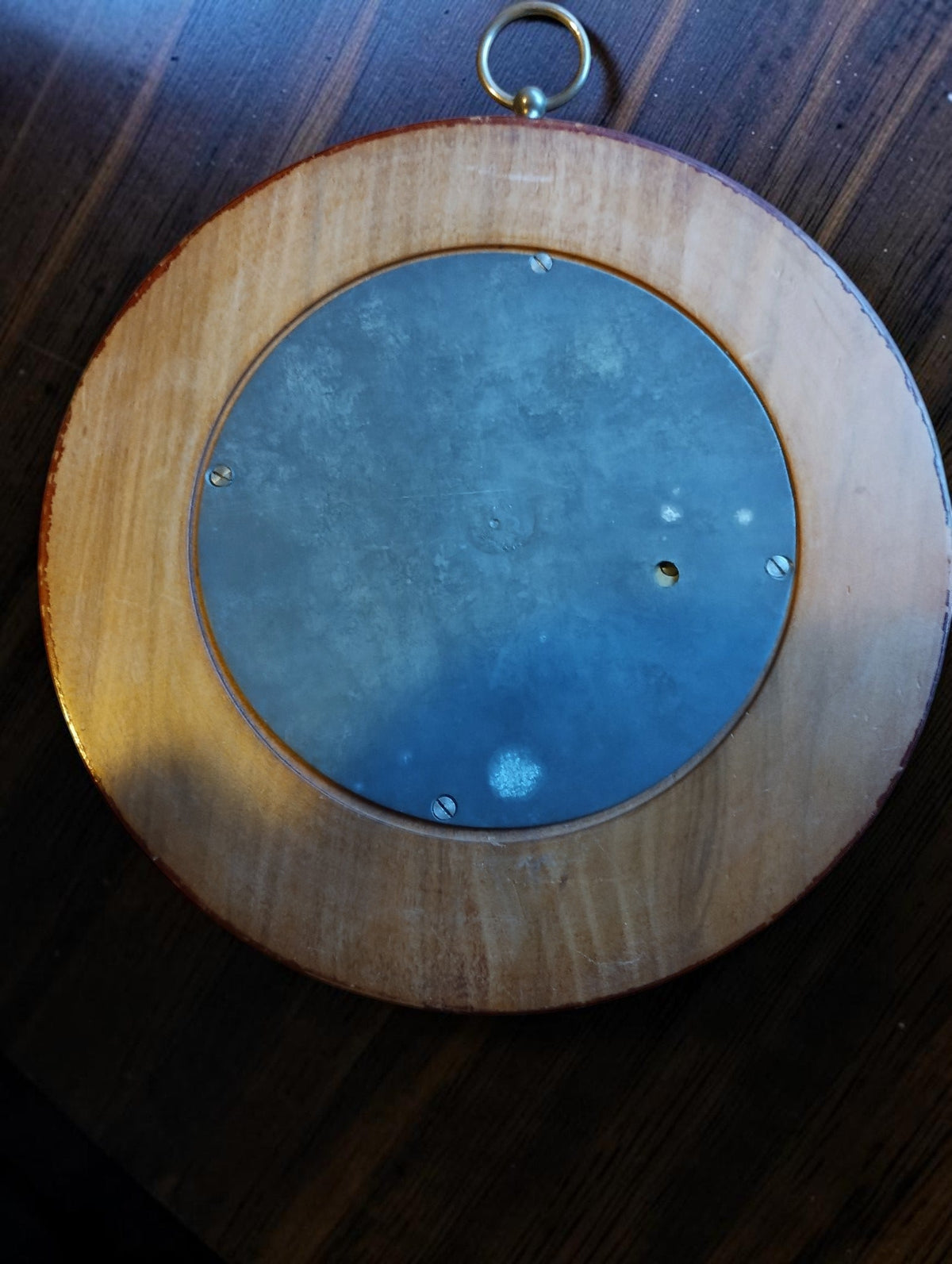 Back of the skeleton barometer with a circular metal cover, fixing screws and surrounding wooden case.
