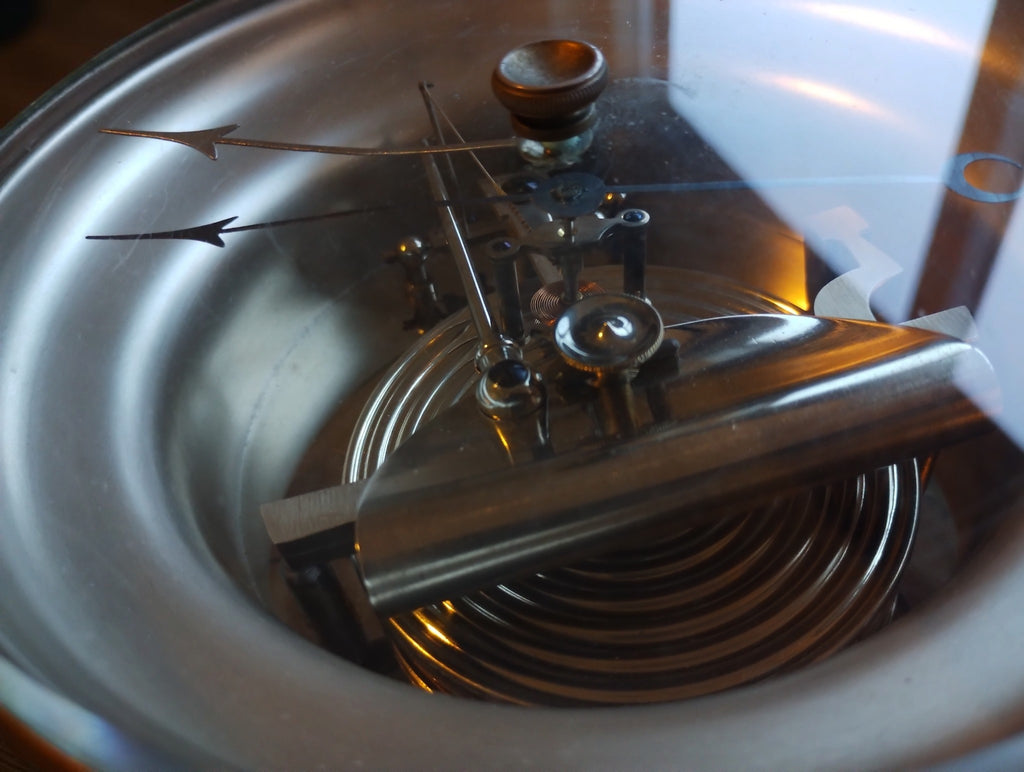 Detailed view through the glass of the barometer pointers, central adjustment knob and exposed mechanism.
