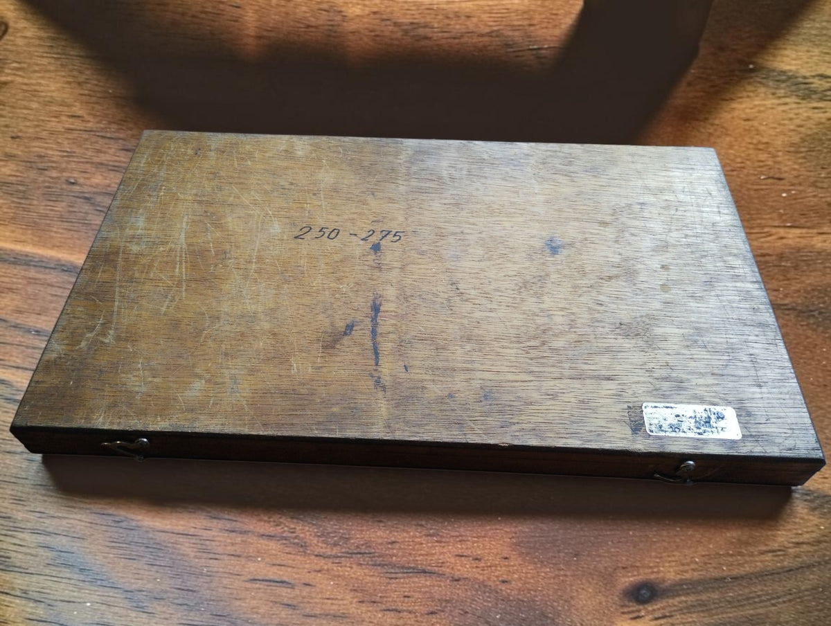 Closed wooden storage case for the NSK 250–275 mm outside micrometer, showing surface wear and handwritten markings.

