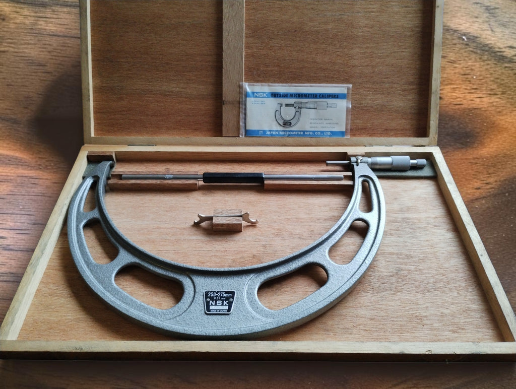 NSK 250–275 mm outside micrometer in its open wooden case with setting standard, adjustment wrench and NSK documentation.

