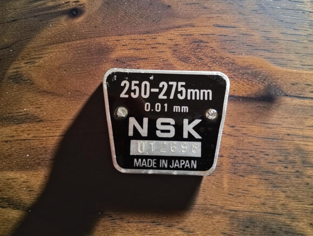 Close-up of the black NSK identification badge marked 250–275 mm, 0.01 mm and Made in Japan, with stamped serial number.

