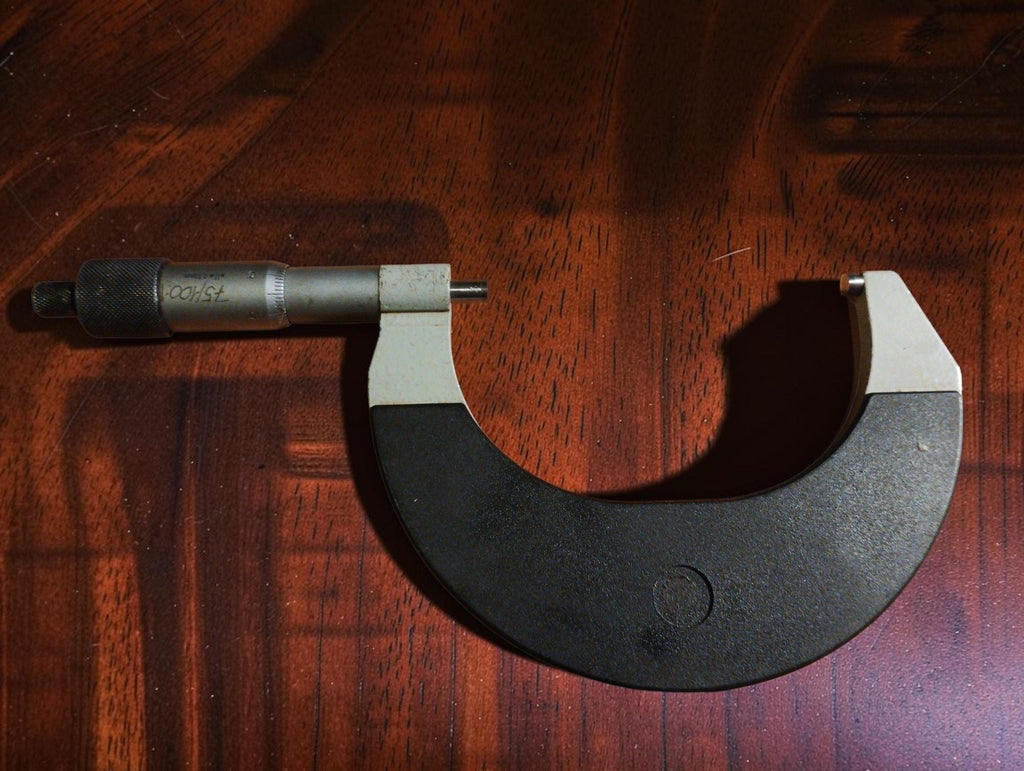 Vintage 75–100 mm outside micrometer with dark frame and metal thimble, shown on a wooden surface.
