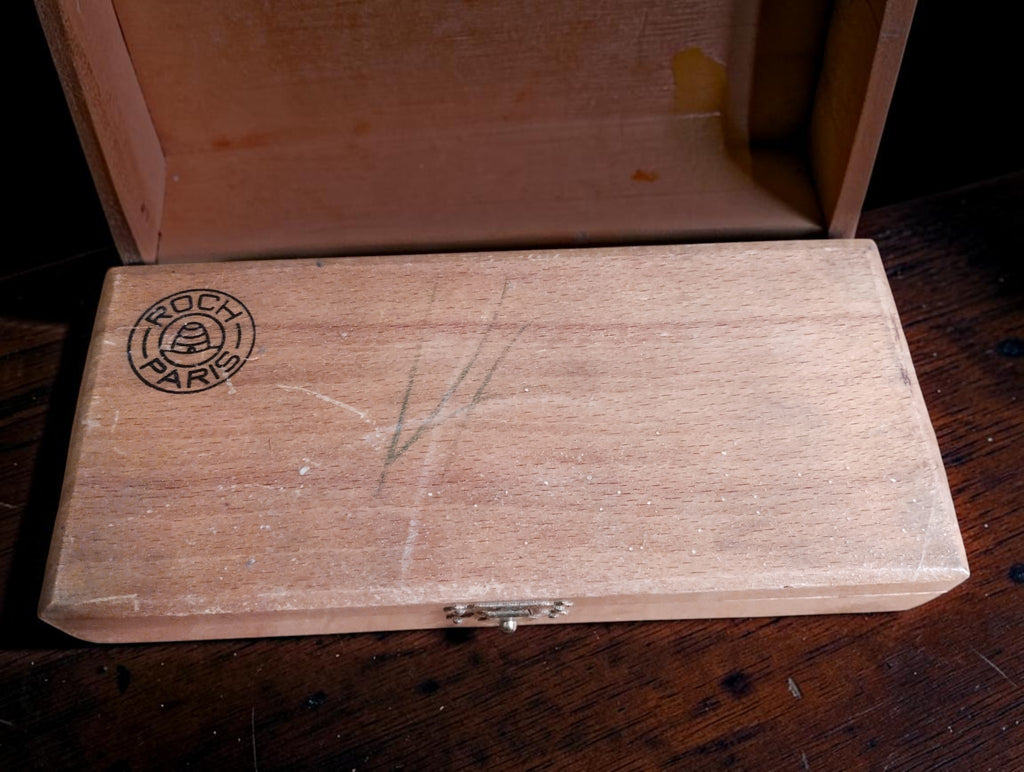 Wooden Roch Paris micrometer case showing the maker's logo, metal clasp and surface wear.
