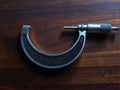 Vintage 75–100 mm outside micrometer with black textured frame and graduated thimble, shown on a wooden surface.
