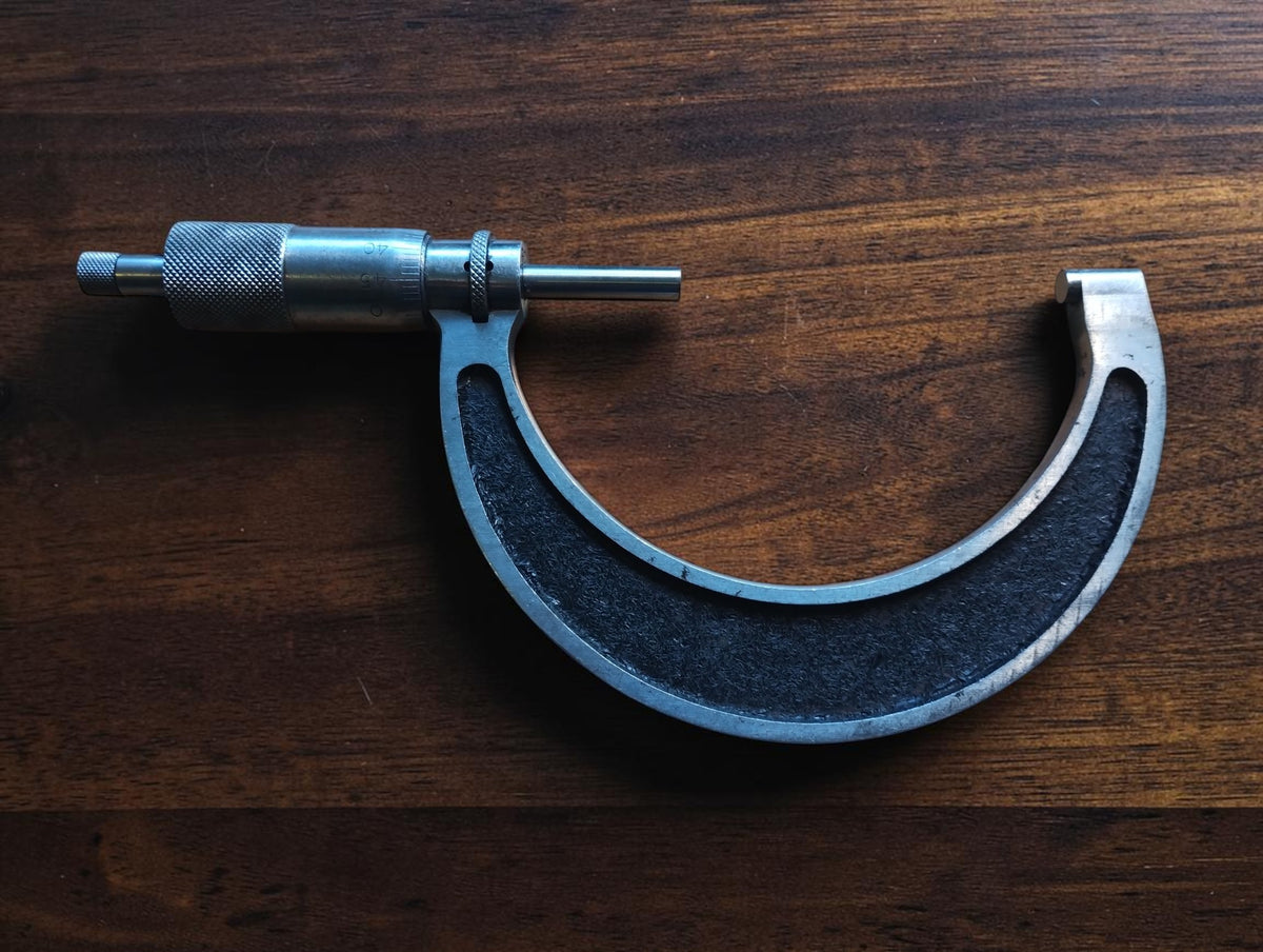 Reverse view of a vintage 75–100 mm outside micrometer showing the curved black frame and metal edges.
