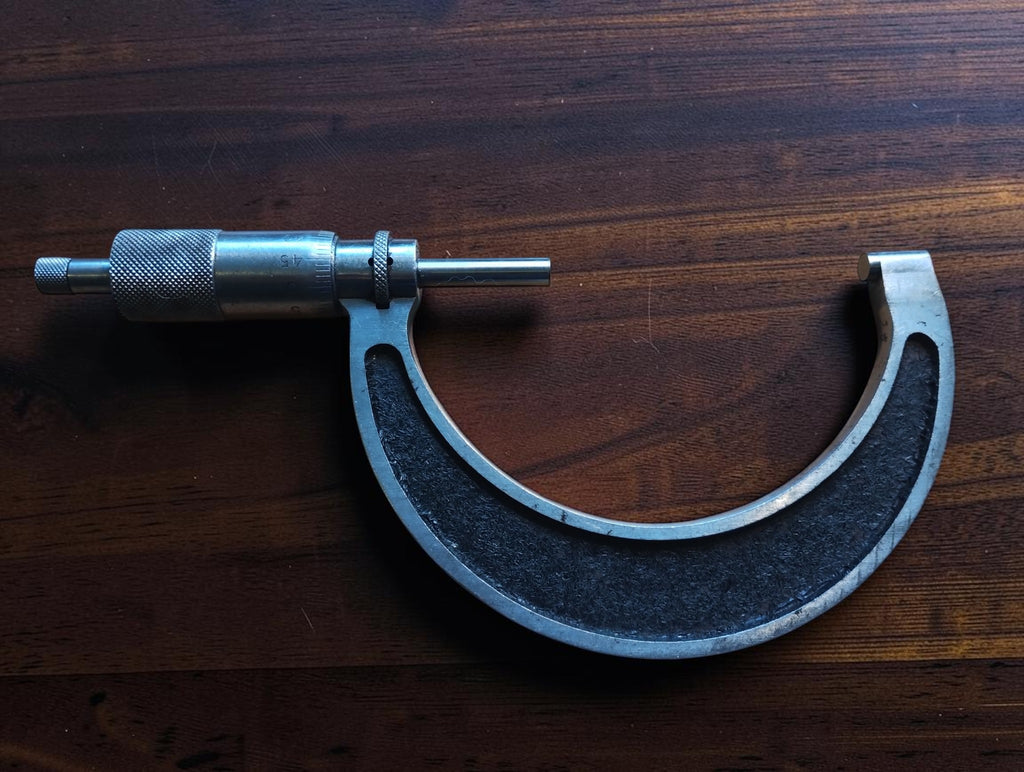Full view of a vintage 75–100 mm outside micrometer with black textured frame and visible signs of use.
