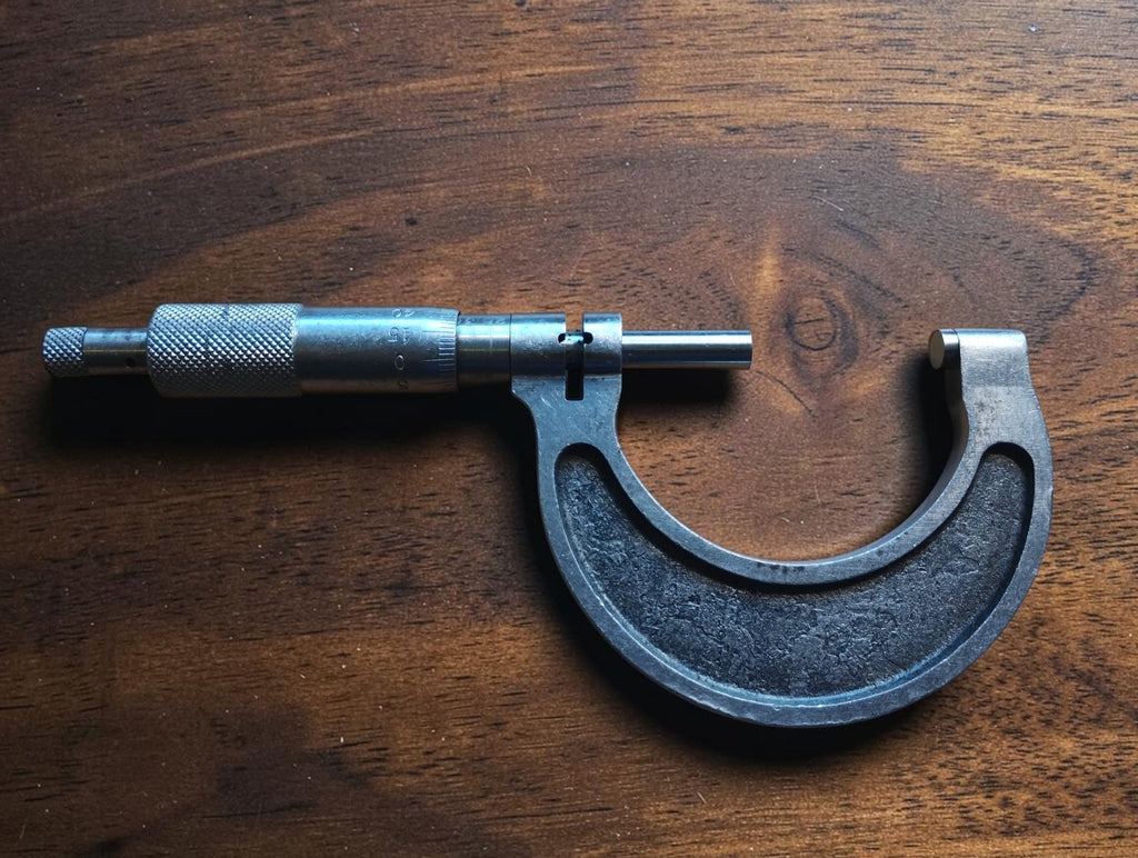 Full side view of a 25–50 mm outside micrometer showing the curved metal frame, spindle and adjustment thimble.
