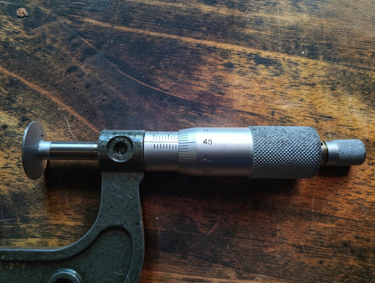 Close-up of the graduated sleeve, rotating thimble and spindle of a vintage disc micrometer.
