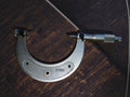 Vintage 75–100 mm outside micrometer with rounded measuring tips, shown vertically on a wooden surface.
