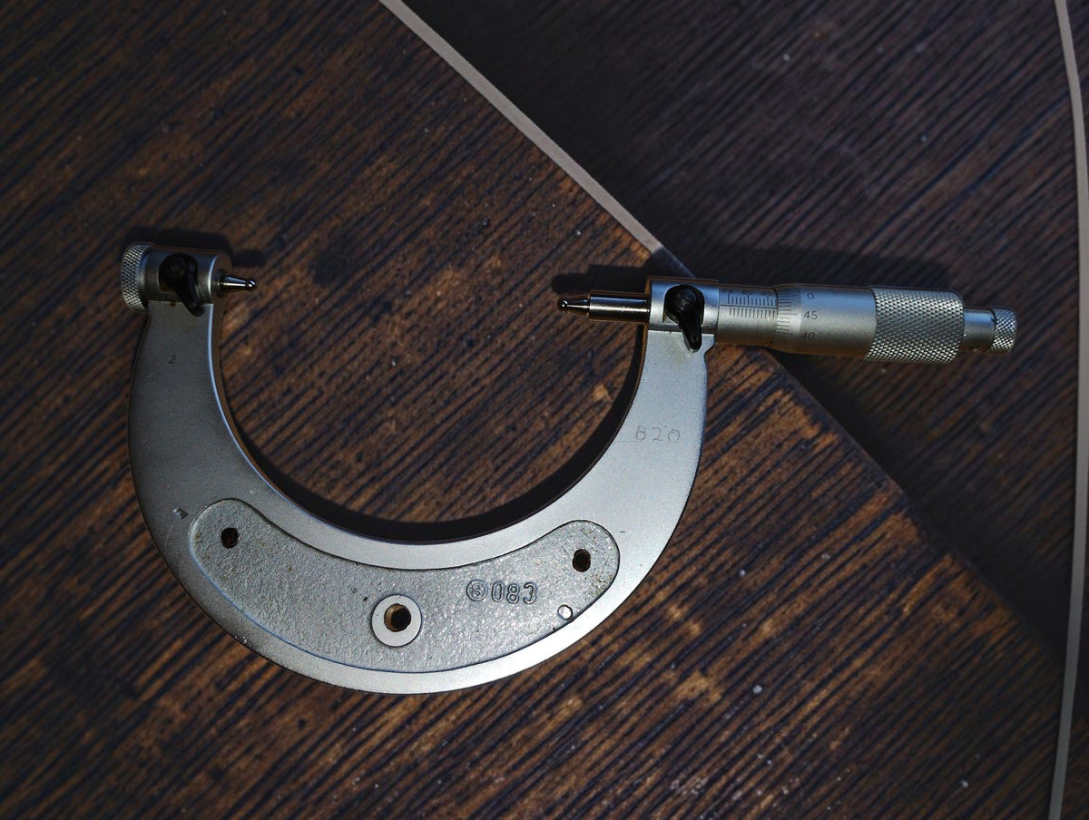 Vintage 75–100 mm outside micrometer with rounded measuring tips, shown vertically on a wooden surface.
