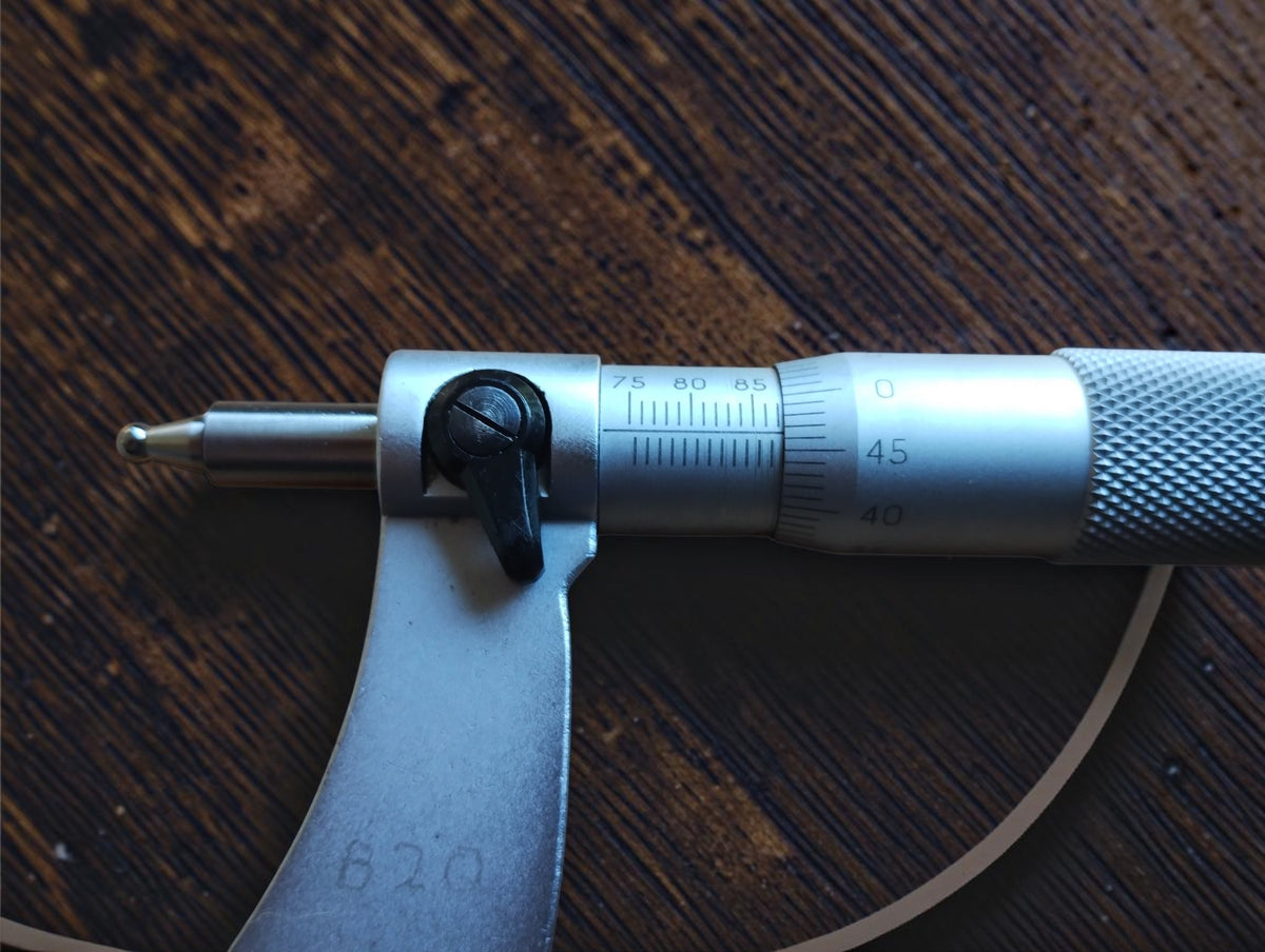 Close-up of the micrometer sleeve scale, graduated thimble, black locking lever and rounded spindle tip.
