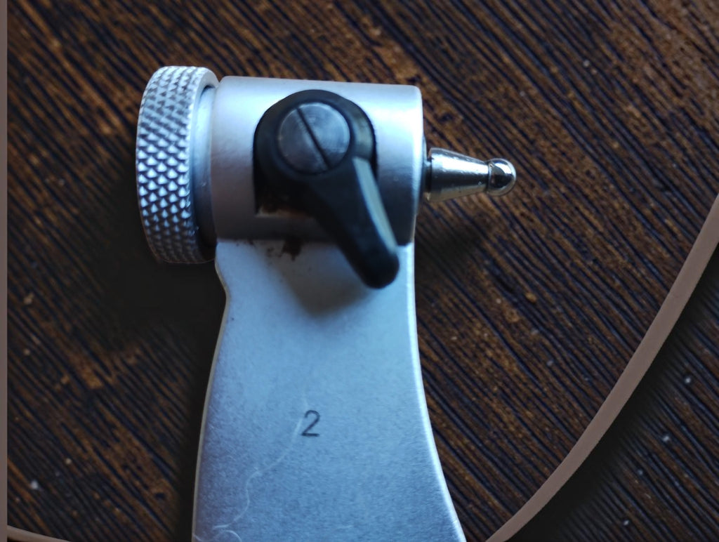 Close-up of a rounded measuring tip, black locking lever and knurled end adjustment on the micrometer frame.
