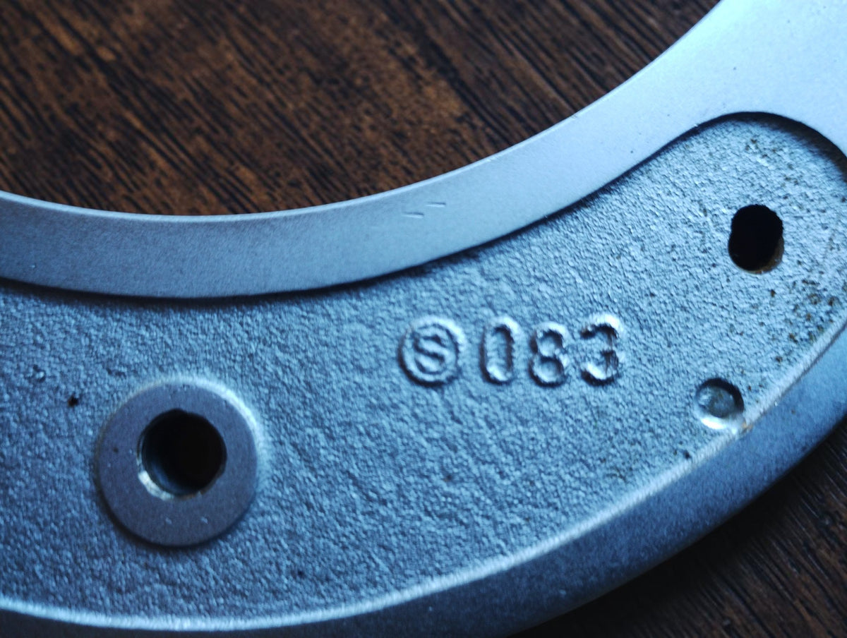 Close-up of the stamped markings and textured metal inset on the vintage micrometer frame.
