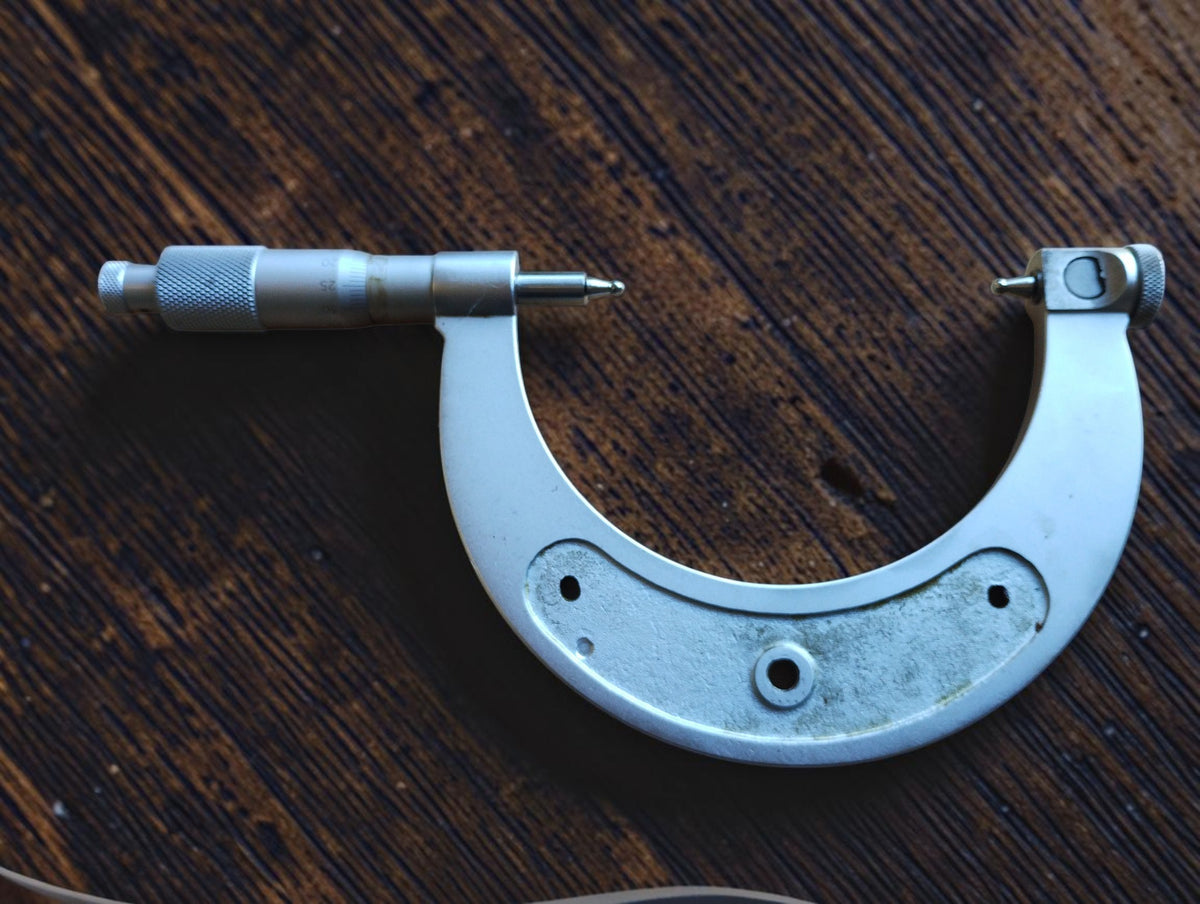 Reverse view of the outside micrometer showing its metal frame, rounded measuring tips and knurled adjustment thimble.

