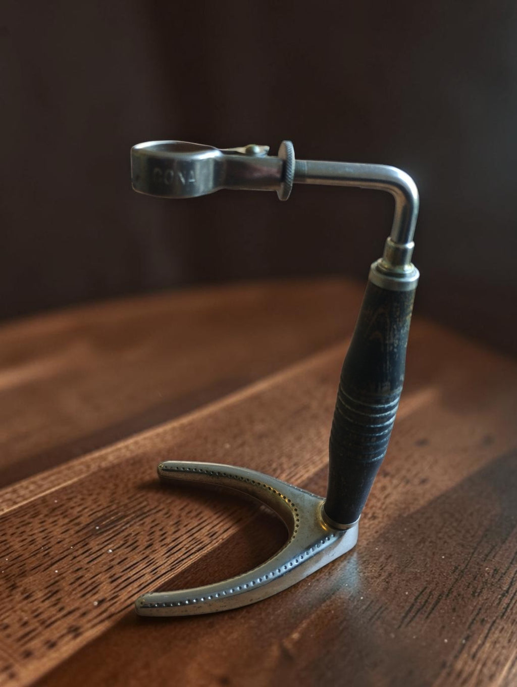 Vintage CONA stamp with dark turned wooden handle, metal arm with spring clip, and perforated wishbone-shaped base, full view
