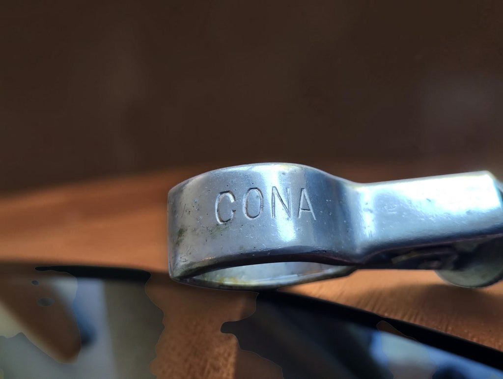 Close-up of the engraved CONA marking on the metal spring clip of a vintage stamp
