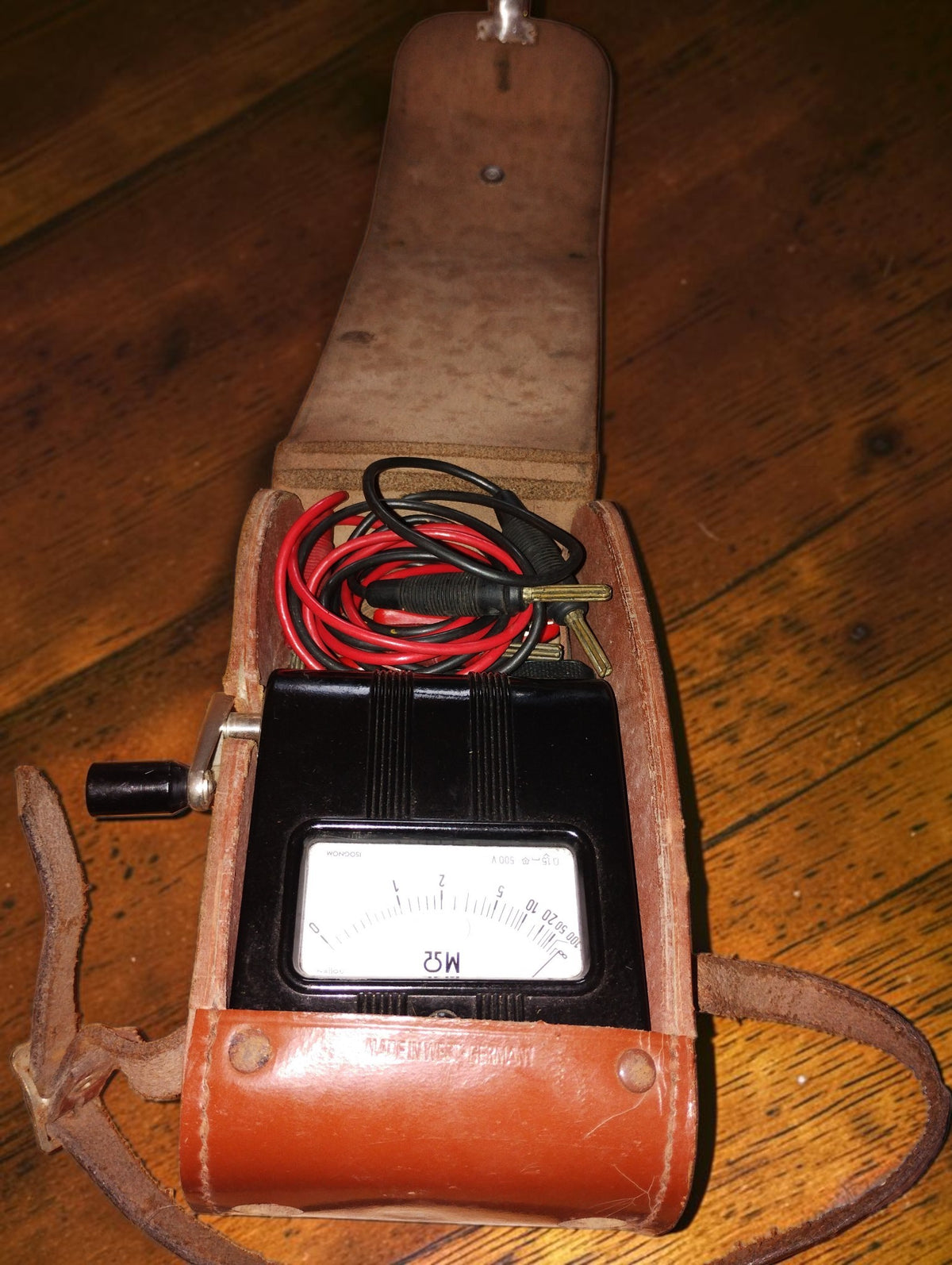 Gossen ISOGNOM insulation tester inside its open leather carrying case, with test leads stored above the analog dial.

