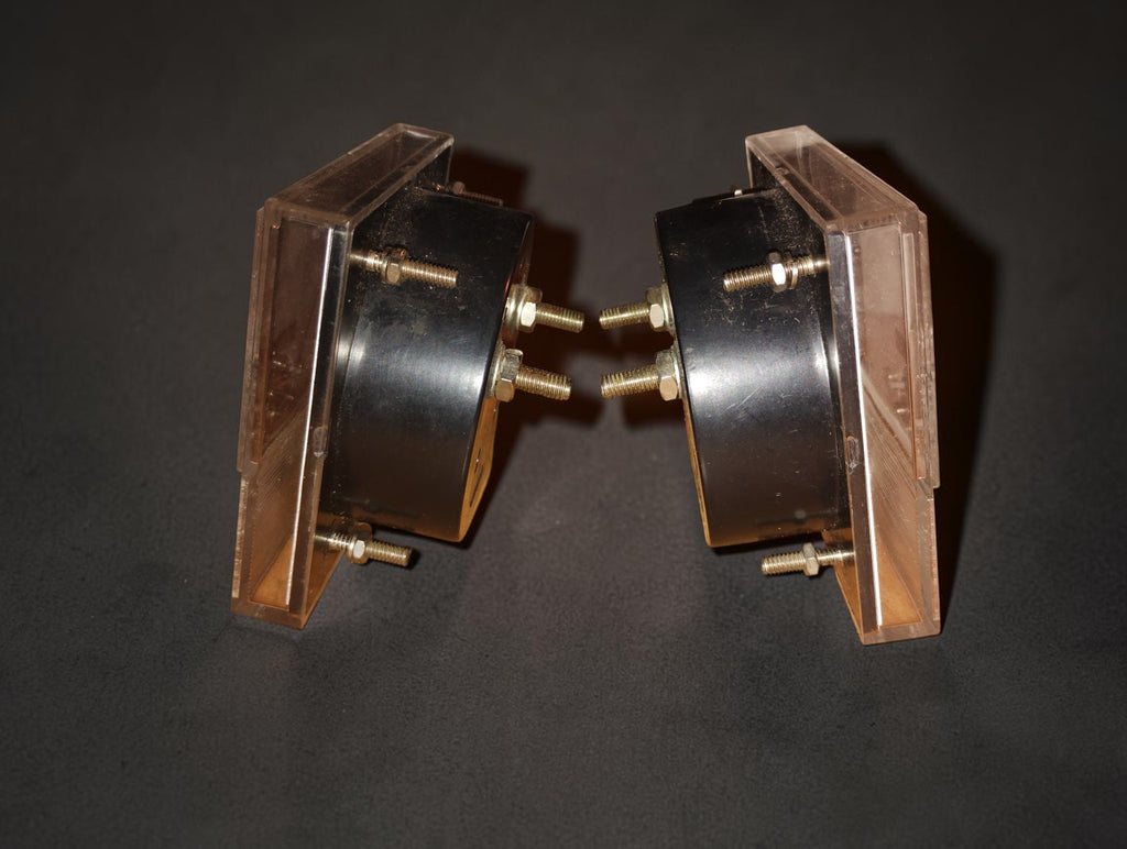 Side view of the two vintage panel meters showing black housings, transparent fronts and mounting studs
