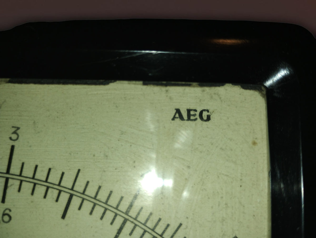 Close-up of the AEG name and fine scale markings on the aged ivory-colored ammeter dial.
