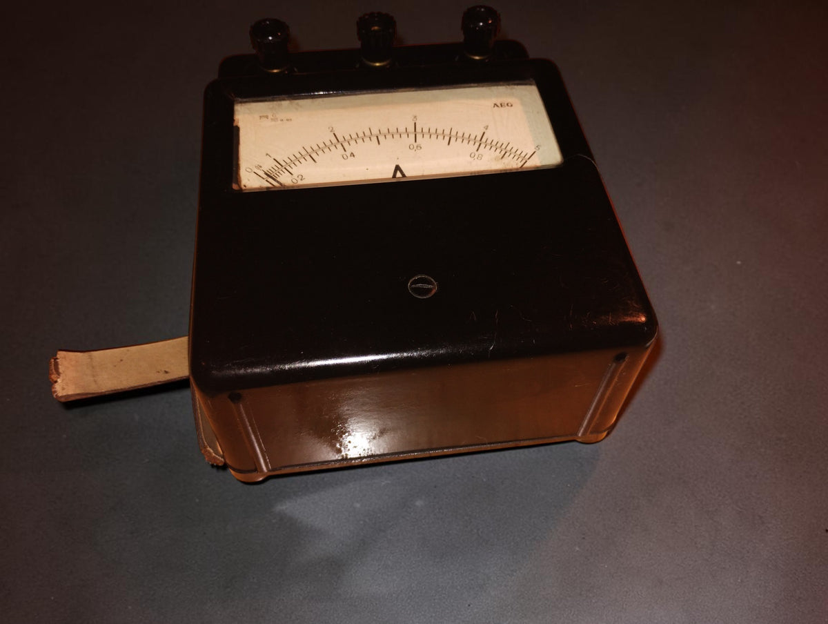 Angled view of the vintage AEG ammeter showing its deep housing, carrying strap, and black instrument face.

