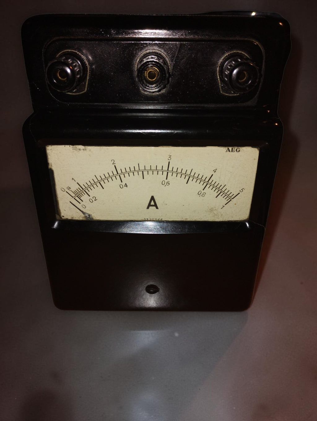 Front view of the vintage AEG ammeter showing three terminals, an ivory-colored dial, and visible signs of age.
