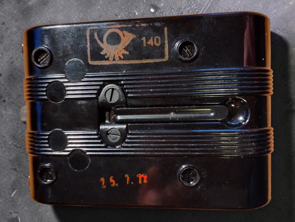 Back of a vintage Bundespost ohmmeter with German post horn emblem, number 140 and orange inspection date stamp
