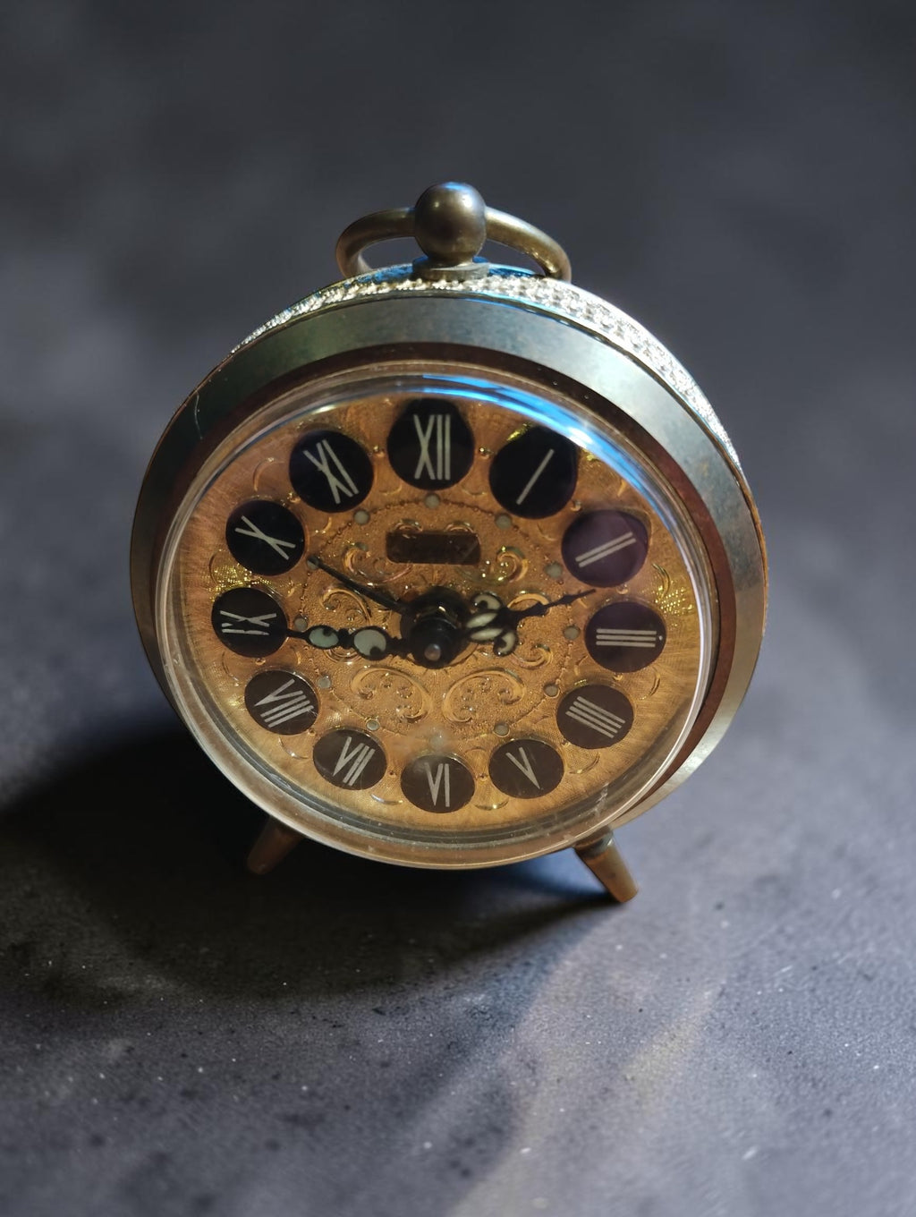 Vintage Jerger mechanical brass alarm clock with an ornate gold-tone dial, Roman numerals and a top carrying ring.
