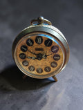 Vintage Jerger mechanical brass alarm clock with an ornate gold-tone dial, Roman numerals and a top carrying ring.

