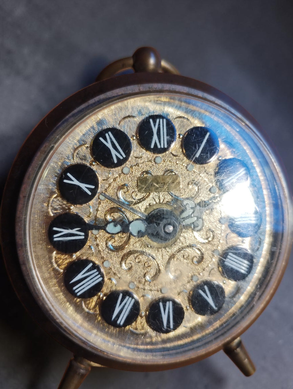 Close-up of the Jerger alarm clock dial with decorative filigree, Roman numeral hour markers and ornate hands.
