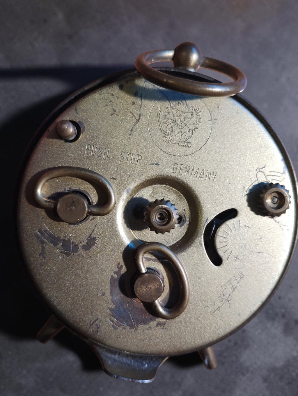 Back of the Jerger mechanical alarm clock with the lion emblem, Push Stop and Germany markings, winding keys and visible wear.
