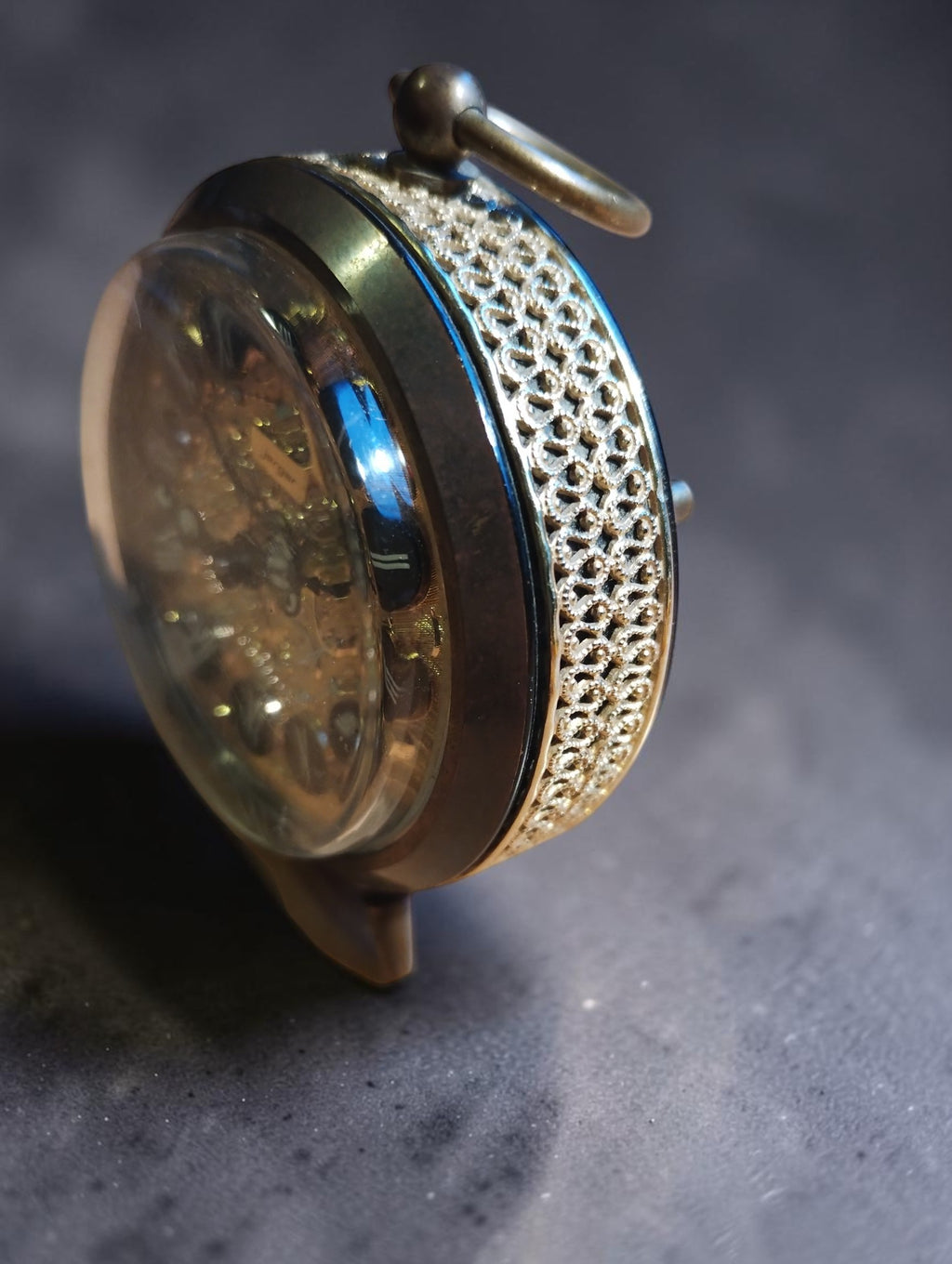 Angled view of the Jerger brass alarm clock showing the openwork case decoration, rounded glass and top carrying ring.
