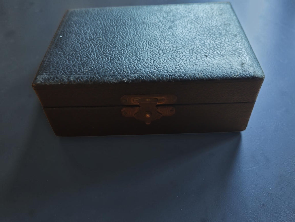 Closed black wooden case with textured covering and metal clasp for the mainspring winder set
