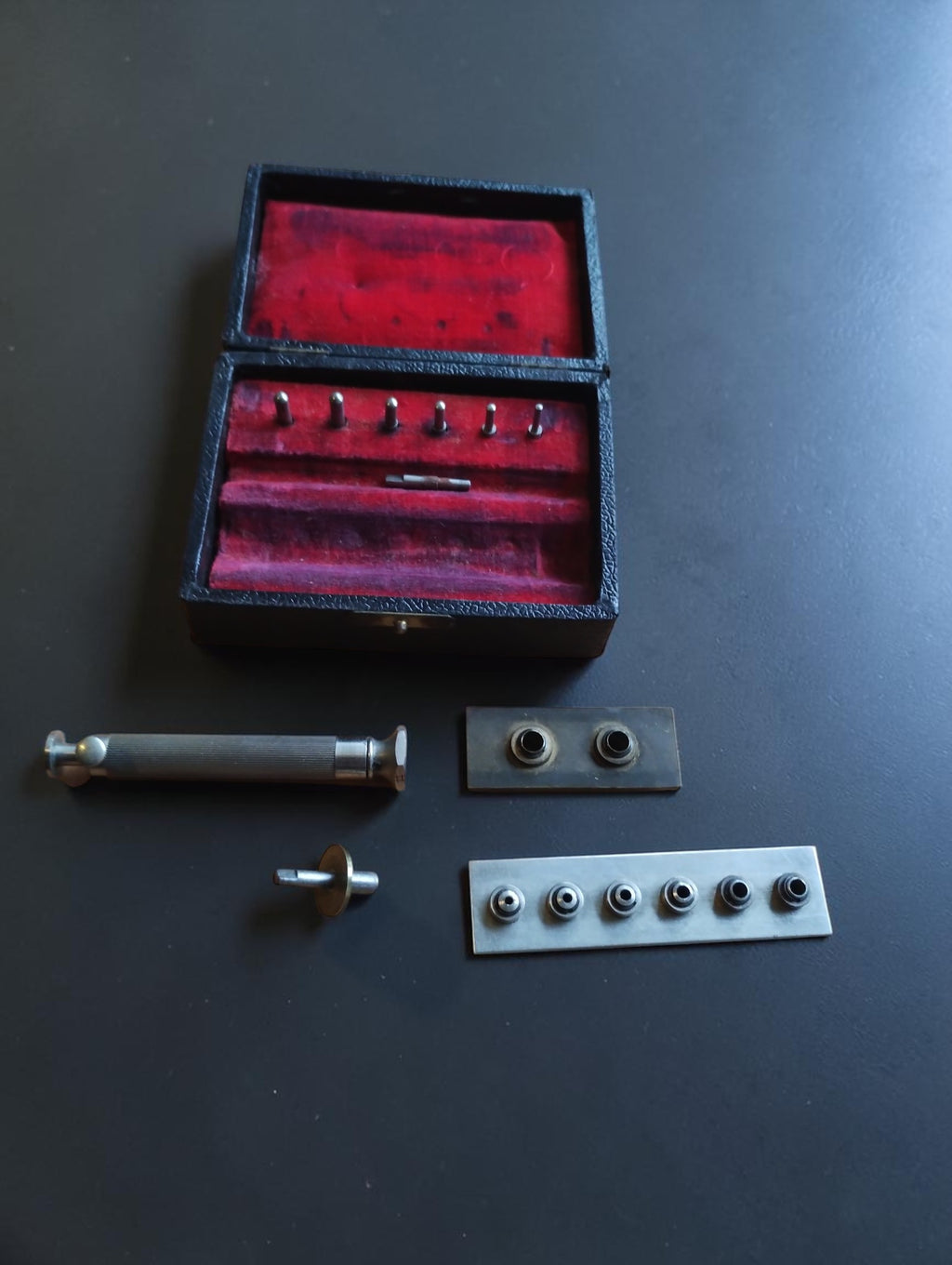 Pocket watch mainspring winder set with arbors and drums arranged beside the open case
