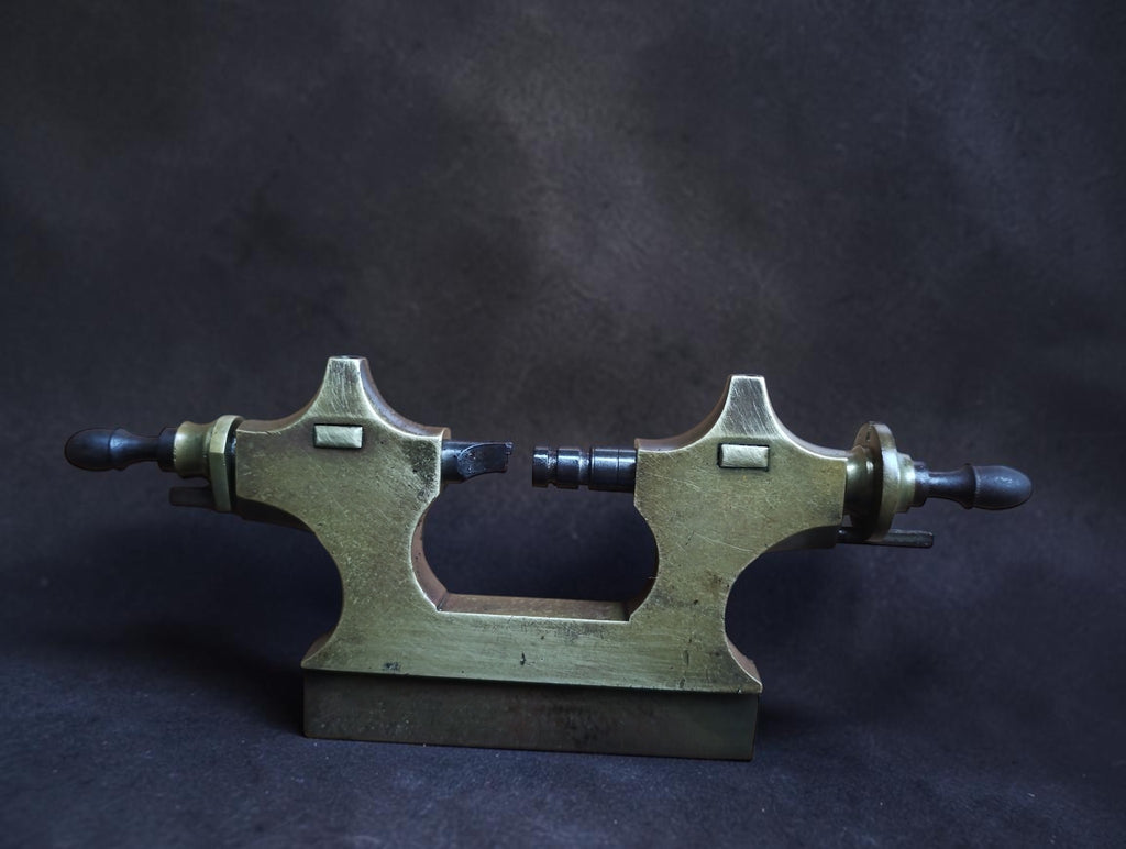 Antique Jacot tool brass frame standing upright with two opposing steel runners and dark wooden handles
